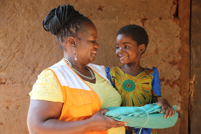 Chimwemwe Mizaya, a World Vision sponsorship coordinator, handing a mosquito net to Thandizo for her family.
