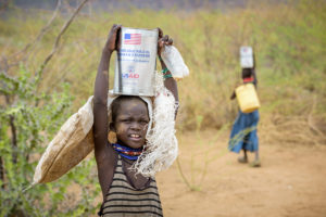 Families leave World Vision food distribution with bags of maize and cans of cooking oil provided by USAID in Turkana, Kenya. ©2017 World Vision, Jon Warren.