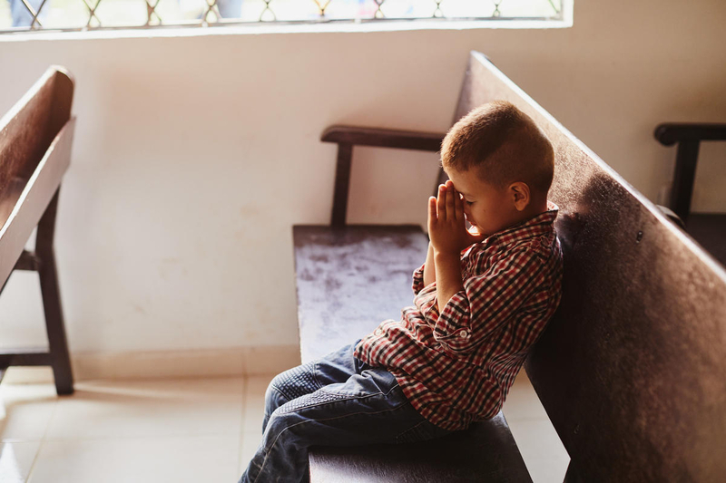 Young boy prays on empty church pew